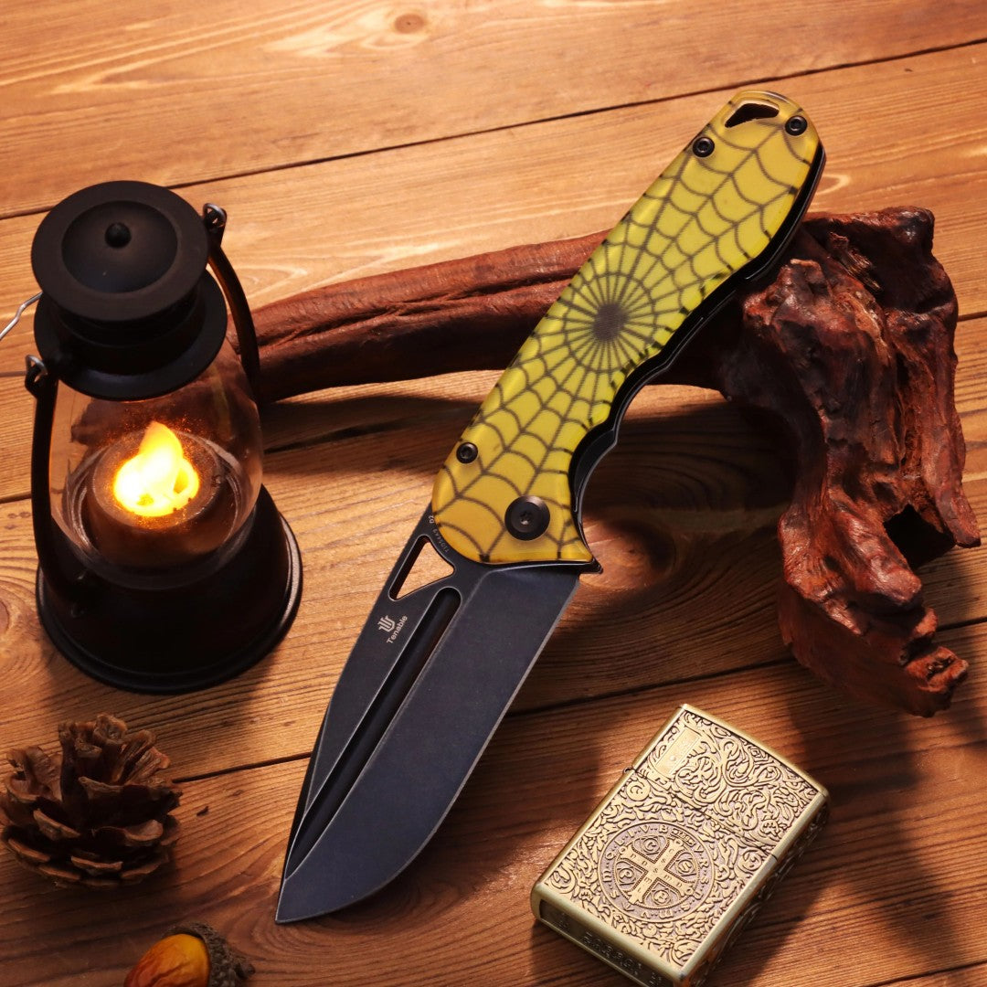 Open Bombur T1054A9 Halloween folder with yellow spiderweb PC handle and blackwash D2 blade on a dark wooden table